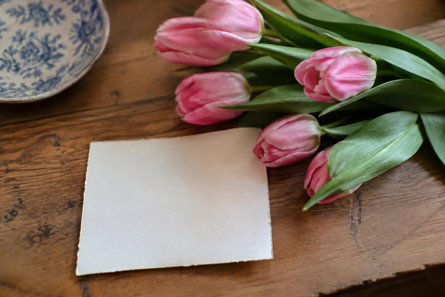 Carte manuscrite posee a plat pres de tulipes roses