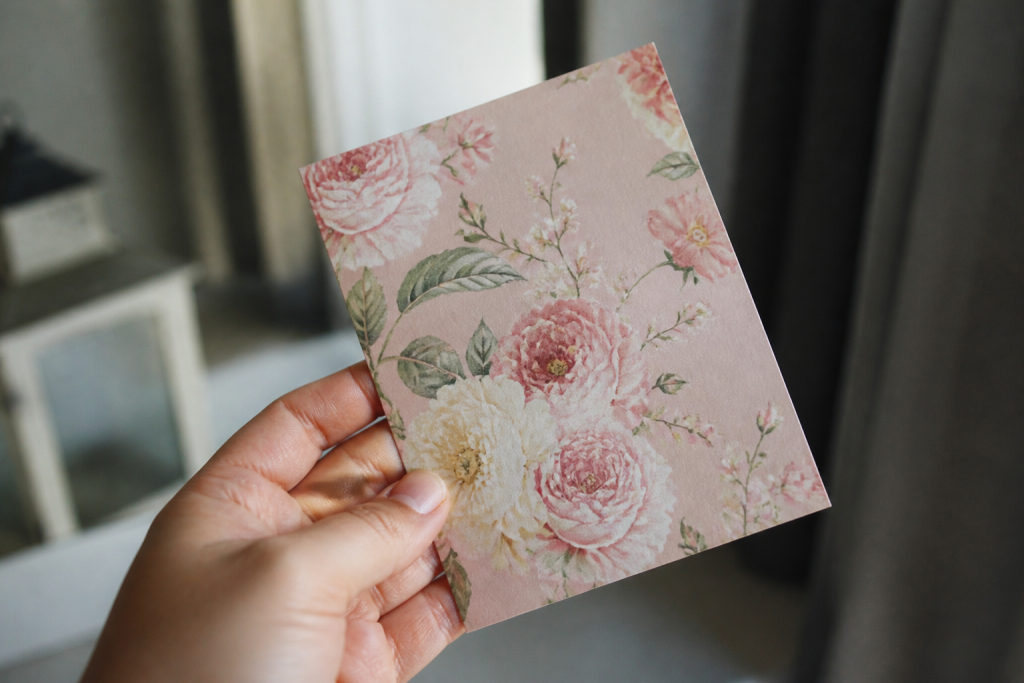 Une main tient une carte rose ornee de fleurs