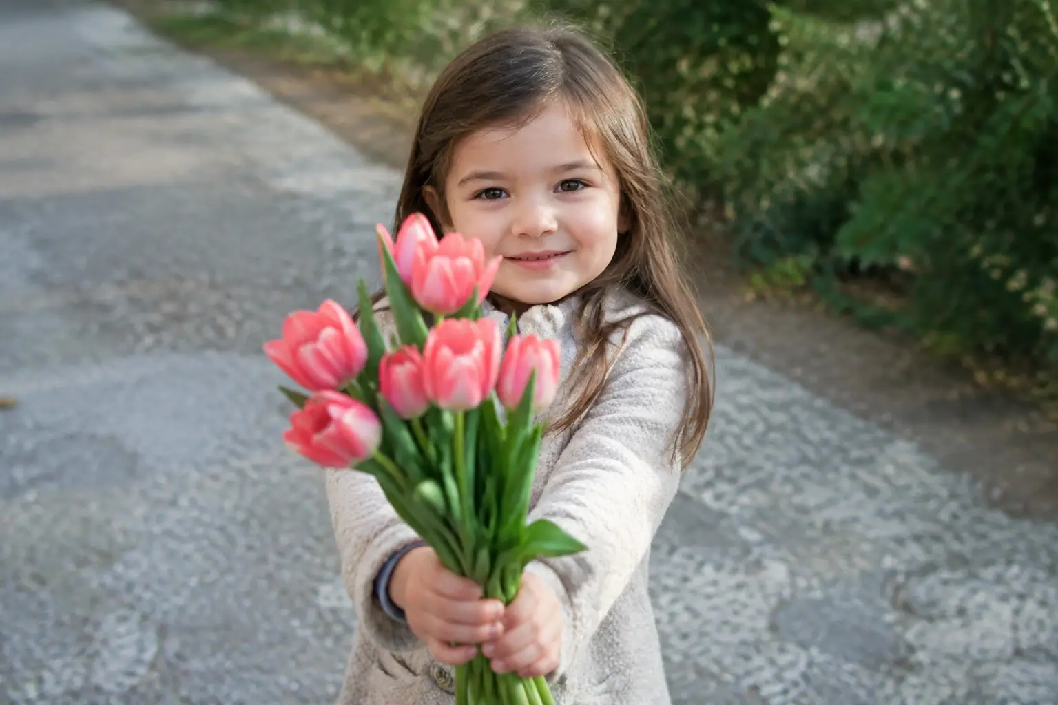 Petite fille debout tendant un bouquet de tulipes roses